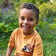 Kaïs a rejoint le concours — aidez-le/la à gagner de superbes lots ! child, boy, smiling, outdoor, garden, greenery, mickey_mouse, tshirt, short_sleeve, happy, cute, portrait, young, casual_clothing, nature, daylight, sitting, curly_hair, playful, bright