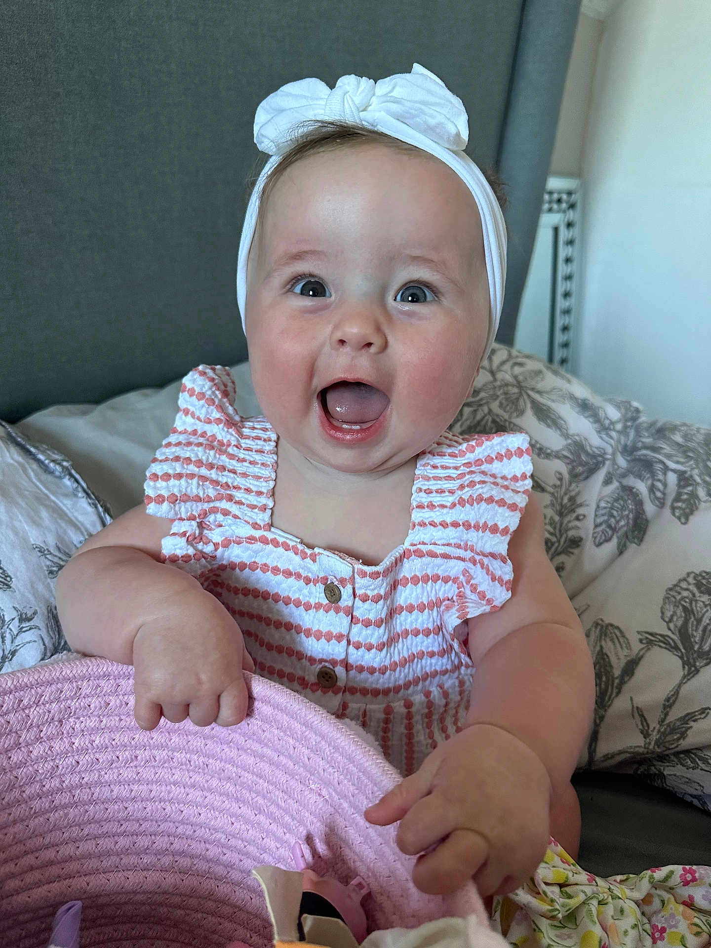 Harper joined the competition — help win amazing prizes! baby, child, headband, bow, smiling, happy, basket, pink, striped_dress, sitting, bed, pillow, floral, indoors, cute, infant, holding, playful, portrait, joyful