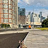 dog, french_bulldog, sidewalk, urban, cityscape, buildings, skyscrapers, leash, pavement, street, blue_sky, clouds, daytime, pet, canine, small_dog, sitting, outdoor, modern_architecture, quiet