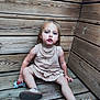 bare_arms, bare_legs, casual, child, curly_hair, dress, expression, face, innocent, natural_light, outdoor, planks, sandals, sitting, small_person, stuffed_animal, toddler, toy, wood, wooden_deck