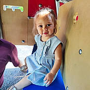Elena a rejoint le concours — aidez-le/la à gagner de superbes lots ! blue_bench, buttoned_dress, casual_clothing, child, colorful_background, curious, girl, happy, indoor_play, light_spot, metal_rivets, play_structure, playground, sandals, seated, short_hair, smile, striped_dress, toddler, young_child