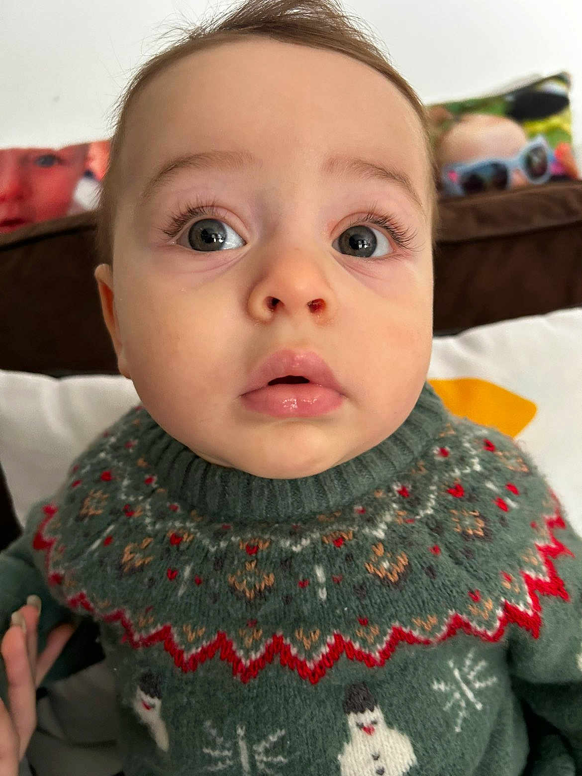 Aïssa a rejoint le concours — aidez-le/la à gagner de superbes lots ! baby, child, face, sweater, green_sweater, snowman, patterned_clothing, close_up, curious_expression, indoor, couch, pillow, colorful_pillow, eyelashes, mouth, head, skin, person, portrait, winter_clothing
