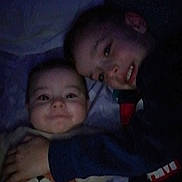 Aïssa a rejoint le concours — aidez-le/la à gagner de superbes lots ! child, baby, smile, face, hug, dark, bed, pillow, clothing, sleeve, person, infant, toddler, cuddle, happy, portrait, indoor, sibling, cozy, sleepwear