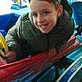 amusement_park, boy, casual_clothing, child, colorful, entertainment, fun, happy, indoor, jacket, leisure, people, playful, portrait, ride, seat, smiling, steering_wheel, toy_car, young
