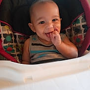 Salem is registered to the contest to win money with this photo: baby, child, high_chair, smile, finger_in_mouth, indoor, seat_cover, colorful, pattern, floral, clothing, person, cute, happy, face, head, young_child, infant, sitting, playful