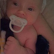 Connor is registered to the contest to win money with this photo: baby, pacifier, infant, blanket, arm, hand, face, headband, skin, sleepy, closeup, newborn, child, person, soft_light, indoors, cuddle, comfort, portrait, resting