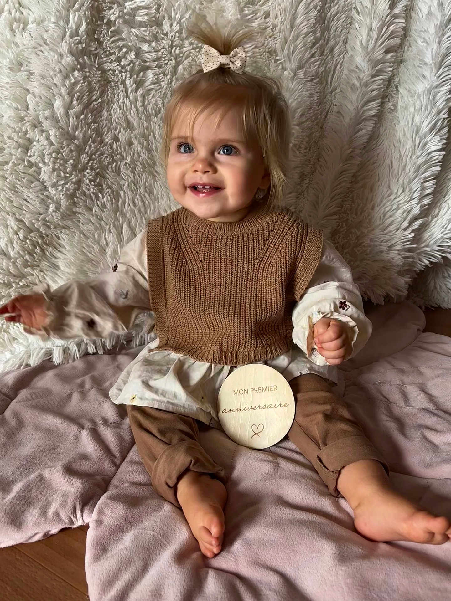 ève participe au concours pour gagner de l'argent avec cette photo : toddler, child, smiling, blue_eyes, hair_bow, brown_clothing, knit_vest, plush_blanket, soft_texture, wooden_plaque, first_birthday, sitting, indoors, happy, cute, portrait, baby, floor, cozy, celebration
