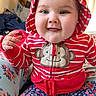 baby, child, infant, portrait, smiling, happy, hooded_outfit, striped_clothing, red_clothing, monkey_patch, floral_pants, sitting, indoors, cushion, couch, colorful, close_up, face, hand, family_photo