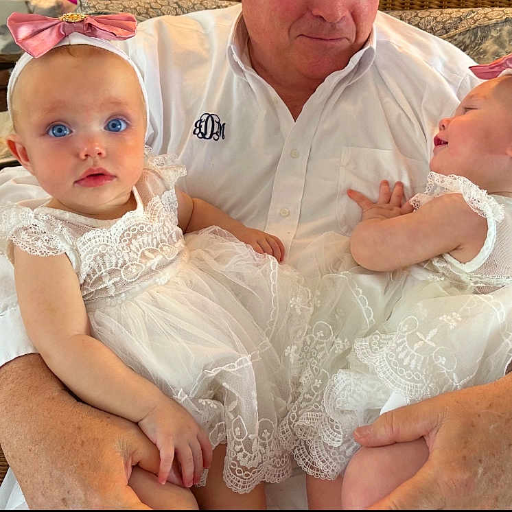 Caramia is registered to the contest to win money with this photo: adult, arms, babies, baby, child, curious, cute, family, headband, holding, indoor, infant, lace, person, pink_bow, portrait, smiling, toddler, white_dress, wicker_chair