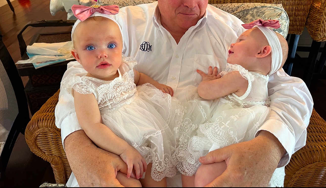 Caramia is registered to the contest to win money with this photo: baby, babies, child, infant, white_dress, lace, headband, pink_bow, adult, arms, wicker_chair, indoor, smiling, curious, portrait, cute, family, toddler, holding, person