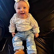 Sayla is registered to the contest to win money with this photo: baby, black_background, bow, brown_shoes, child, couch, cute, denim, happy, headband, indoor, infant, jeans, lace, patch, person, portrait, sitting, smiling, white_clothing