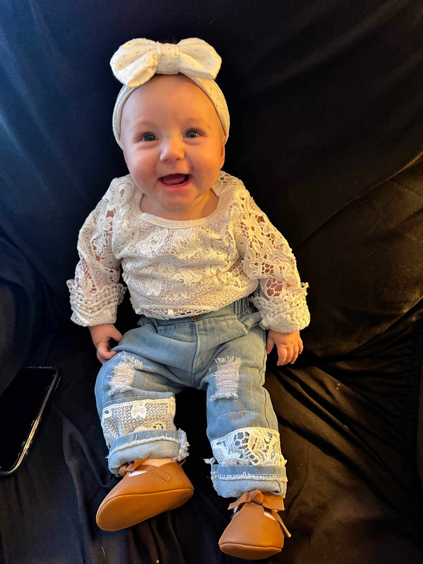 Sayla is registered to the contest to win money with this photo: baby, black_background, bow, brown_shoes, child, couch, cute, denim, happy, headband, indoor, infant, jeans, lace, patch, person, portrait, sitting, smiling, white_clothing