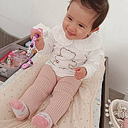 Mya a rejoint le concours — aidez-le/la à gagner de superbes lots ! baby, child, smiling, toy, sitting, pink_pants, white_top, collar, beaded_toy, changing_pad, indoor, happy, cute, infant, playful, soft_lighting, baby_essentials, basket, sock, wooden_furniture