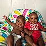 baby, infant, smile, diaper, onesie, red_clothing, colorful_blanket, patterned_blanket, happy, cute, two_babies, sitting, indoors, wall, skin, chubby_cheeks, child, portrait, family, toddler