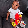 Lujuan Oshea joined the competition — help win amazing prizes! baby, child, plush_toy, elmo, couch, onesie, socks, indoor, toy, person, face, sitting, cute, infant, soft_toy, expression, furniture, hands, leg, room