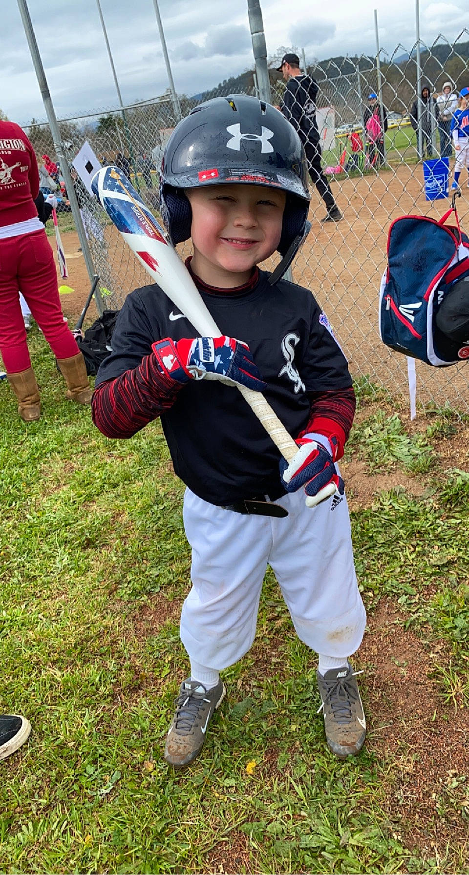 John is registered to the contest to win money with this photo: ball_game, baseball_equipment, baseball_player, bat_and_ball_games, football_helmet, fun, glove, grass, headwear, helmet, joy, person, personal_protective_equipment, player, recreation, shoe, smile, sneakers, sports, sports_equipment