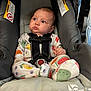 baby, child, car_seat, onesie, fruit_pattern, blue_eyes, chubby_cheeks, seatbelt, cushion, warning_label, infant, clothing, indoor, cute, secure, sitting, person, portrait, closeup, looking_away