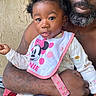 adult, arm, baby, beard, bib, child, closeup, clothing, expression, face, hand, holding, minnie_mouse, outdoor, person, portrait, sitting, skin, tattoos, toddler
