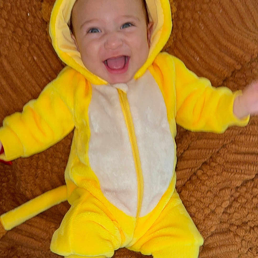 Ynfante Jeanner is registered to the contest to win money with this photo: baby, blanket, child, clothing, cozy, cute, feet, happy, hood, indoor, infant, lion_costume, lying_down, open_mouth, plush, portrait, smiling, socks, toothy_grin, yellow_costume