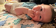 Theo is registered to the contest to win money with this photo: baby, infant, child, blanket, dinosaur_pattern, hand, face, skin, eyes, lying_down, indoors, cozy, soft_light, curious, cute, toddler, sleepwear, carpet, closeup, portrait