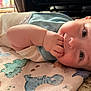 baby, infant, child, blanket, dinosaur_pattern, hand, face, skin, eyes, lying_down, indoors, cozy, soft_light, curious, cute, toddler, sleepwear, carpet, closeup, portrait