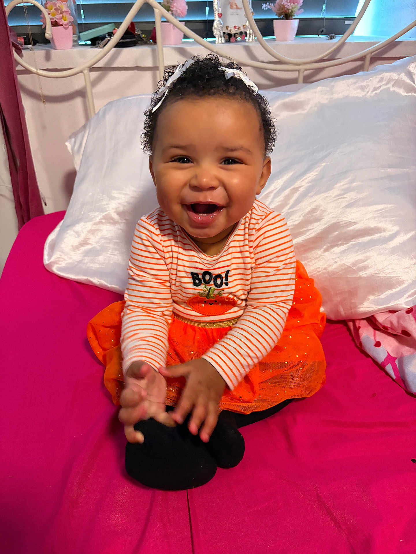 Larissa-Rose is registered to the contest to win money with this photo: baby, child, smiling, happy, orange_clothing, striped_shirt, tutu, bed, pink_bedspread, pillow, indoor, curly_hair, headband, hands, playful, cute, person, home, decor, infant