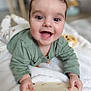 baby, infant, smile, smiling, tummy_time, green_shirt, blanket, toy, wooden_toy, hand, face, big_eyes, cute, lying_down, indoors, portrait, soft_texture, play, nursery, blurred_background