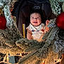 Alex is registered to the contest to win money with this photo: baby, smiling, wreath, christmas, ornaments, lights, car_seat, holiday, festive, infant, happy, face, indoor, decorations, frosted, seasonal, cute, person, celebration, cozy