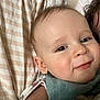 baby, infant, face, smile, cheek, eye, bib, blanket, pillow, bedding, close_up, portrait, person, skin, hair, ear, cuddling, soft_texture, home, adorable