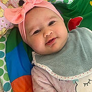 Lúcia a rejoint le concours — aidez-le/la à gagner de superbes lots ! baby, bib, blanket, child, clothing, colorful, cozy, cute, face, happy, headband, indoors, infant, lying_down, pink_bow, play_mat, portrait, smile, soft_toy, young