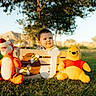 baby, child, plush_toy, tigger, winnie_the_pooh, wooden_crate, grass, outdoor, sunlight, tree, mountains, letter_j, bee_decorations, cute, smiling, daylight, nature, park, toy, portrait