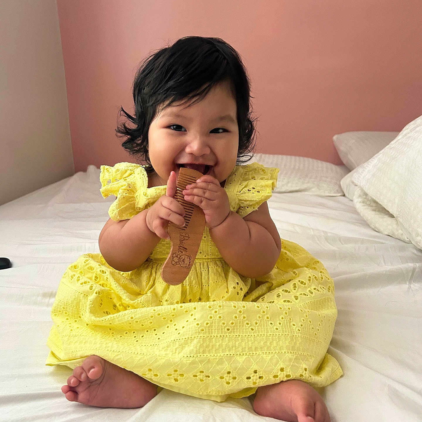 Brielle joined the competition — help win amazing prizes! baby, child, yellow_dress, comb, bed, smiling, happy, indoor, portrait, cute, infant, person, sitting, furniture, pink_wall, soft_lighting, hands, feet, hair, playful