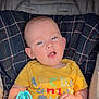 baby, infant, child, stroller, onesie, toy, teether, plaid, seat, blue_eyes, yellow_shirt, alphabet_print, hand, face, head, adorable, sunlight, portrait, phone_overlay, smile
