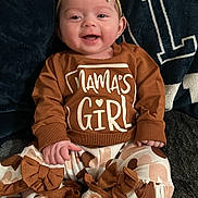 Valkyrie is registered to the contest to win money with this photo: baby, child, smiling, headband, bow, sweatshirt, text_on_clothing, patterned_pants, ruffles, plush_slippers, sitting, indoor, blanket, cozy, portrait, closeup, cute, hands, feet, fabric