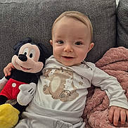Ewen participe au concours pour gagner de l'argent avec cette photo : baby, infant, smiling, mickey_mouse, plush_toy, couch, blanket, pajamas, cute, child, face, hand, soft, indoor, comfort, happy, person, toy, seated, cozy