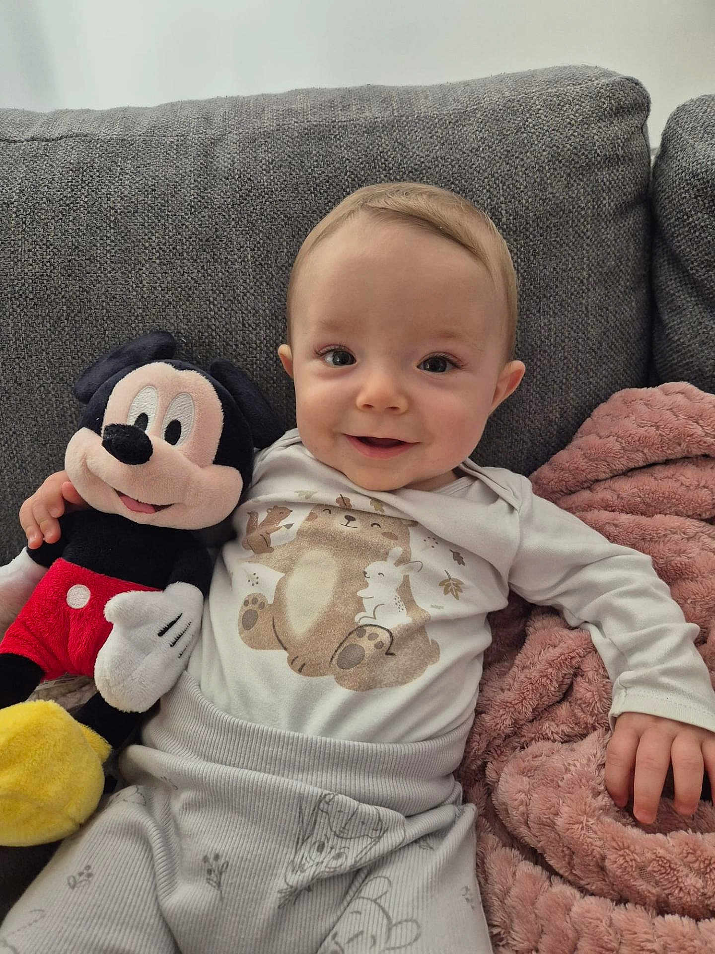 Ewen participe au concours pour gagner de l'argent avec cette photo : baby, infant, smiling, mickey_mouse, plush_toy, couch, blanket, pajamas, cute, child, face, hand, soft, indoor, comfort, happy, person, toy, seated, cozy