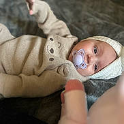 Hanaé a rejoint le concours — aidez-le/la à gagner de superbes lots ! baby, pacifier, knit_hat, knit_outfit, beige_clothing, blanket, infant, child, cute, soft_texture, face, portrait, lying_down, warm_clothing, indoor, headwear, baby_boy, baby_girl, calm, cozy