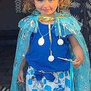 Estelle a rejoint le concours — aidez-le/la à gagner de superbes lots ! child, girl, tiara, cape, blue_clothing, shorts, flower_pattern, wand, curly_hair, smile, earrings, necklace, portrait, costume, playful, indoor, person, cute, fashion, accessories