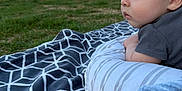 Jayden is registered to the contest to win money with this photo: baby, infant, blanket, pillow, outdoor, grass, people, group, nature, daylight, park, tree, child, curious, side_view, sitting, relaxing, casual, gaze, portrait