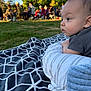 baby, infant, blanket, pillow, outdoor, grass, people, group, nature, daylight, park, tree, child, curious, side_view, sitting, relaxing, casual, gaze, portrait
