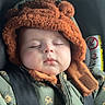 baby, sleeping, car_seat, hat, fur_hat, jacket, green_jacket, animal_print, lion_print, child, infant, seatbelt, strapped_in, closed_eyes, cute, cozy, warm_clothing, no_smoking_sign, indoors, portrait