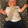 baby, infant, child, white_shirt, navy_pants, star_pattern, mat, lying_down, arms_spread, curious_expression, indoor, cute, small_hands, face, head, feet, skin, person, clothing, baby_garment