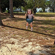 Leah is registered to the contest to win money with this photo: child, toddler, girl, swing, playground, outdoor, park, smiling, portrait, face, striped_shirt, shorts, shoes, socks, trees, pine_trees, sand, grass, houses, sunlight
