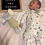 Rj is registered to the contest to win money with this photo: baby, infant, newborn, milestone_sign, letter_board, two_months, onesie, space_print, stuffed_elephant, plush_toy, pink_blanket, soft_blanket, lying_down, smiling, portrait, hand, wooden_frame, nursery, cute, sleepwear