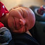 baby, sleeping, red_pajamas, polka_dots, smile, face, infant, cozy, closeup, soft_light, blurred_background, home, comfort, person, newborn, resting, cute, skin, portrait, child