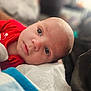 baby, infant, face, eyes, red_clothing, lying_down, portrait, close_up, skin, head, expression, person, young_child, soft_light, indoors, blanket, comfort, cute, peaceful, newborn