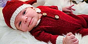 Hezekiah is registered to the contest to win money with this photo: baby, infant, red_hat, red_outfit, knitwear, smile, face, hand, fingers, white_fur, soft_texture, cute, portrait, lying_down, child, cozy, warm_clothing, indoor, closeup, happy