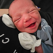 Hezekiah is registered to the contest to win money with this photo: newborn, baby, smile, happy, infant, cute, face, mittens, clothing, closeup, portrait, sleepy, soft, warm, skin, expression, human, person, joy, cozy