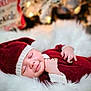 baby, sleeping, red_hat, red_clothing, knitwear, blanket, soft_texture, holiday_lights, festive, blurred_background, cozy, infant, cute, peaceful, portrait, indoors, child, smiling, resting, warm