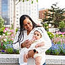 baby, mother, child, infant, portrait, outdoor, garden, flowers, tulips, city, urban, family, parenting, smiling, white_dress, white_clothing, headband, socks, trees, buildings